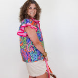 Woman wearing a colorful patterned shirt and white shorts against a white background