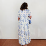 Woman wearing a blue and white floral dress against a white wall.