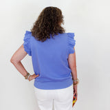 Person wearing a blue top with ruffled shoulders against a white background