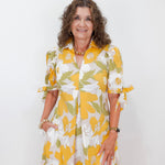 Woman wearing a yellow and white floral dress against a white background