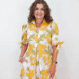 Woman wearing a yellow and white floral dress against a white background