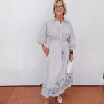 Woman wearing a light gray dress with floral patterns against a white wall.