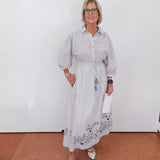 Woman wearing a light gray dress with floral patterns against a white wall.