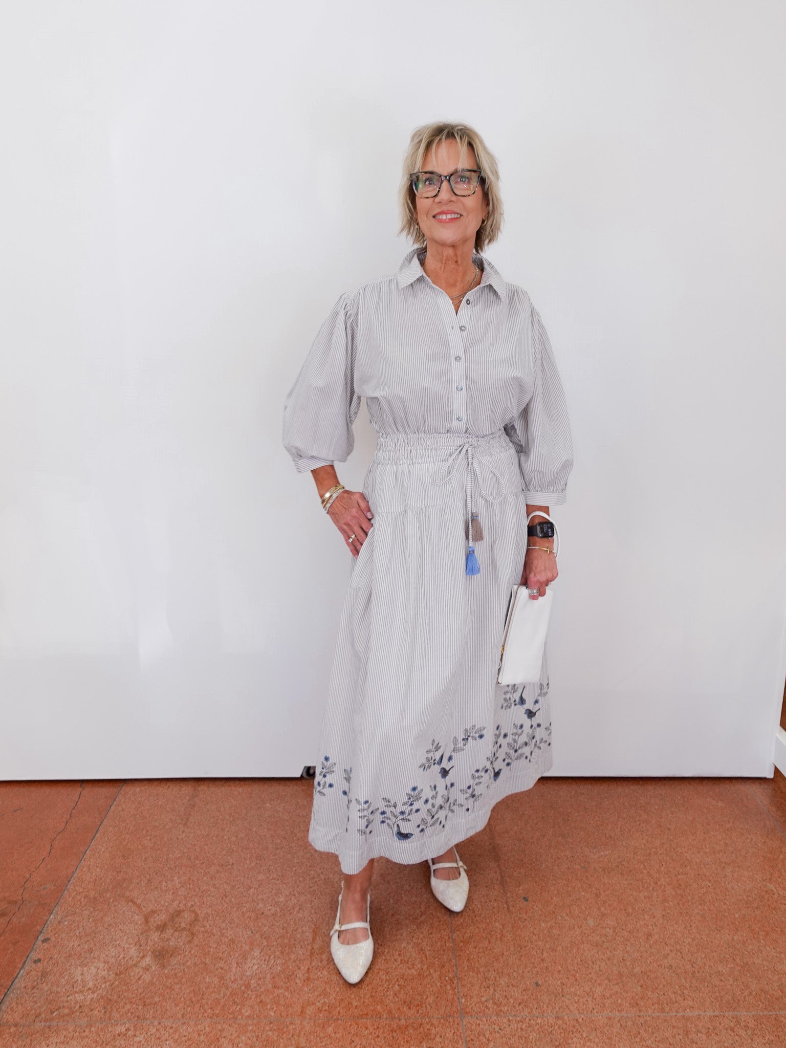 Woman wearing a light gray dress with floral patterns against a white wall.