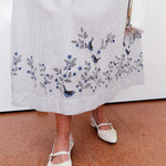 Person wearing a white dress with floral embroidery and white shoes on a red floor.