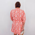 Person wearing a red floral dress against a white wall