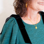 Person wearing a green sweater with a black strap over one shoulder, gold necklace, and earrings.