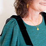 Person wearing a green sweater with a black strap over one shoulder, gold necklace, and earrings.