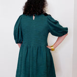 Person wearing a teal dress with puffed sleeves against a white background