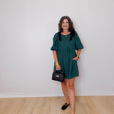 Woman wearing a green dress with black accents against a white wall.