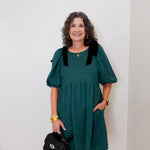 Woman wearing a teal dress with black accents against a white wall