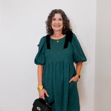 Woman wearing a teal dress with black accents against a white wall