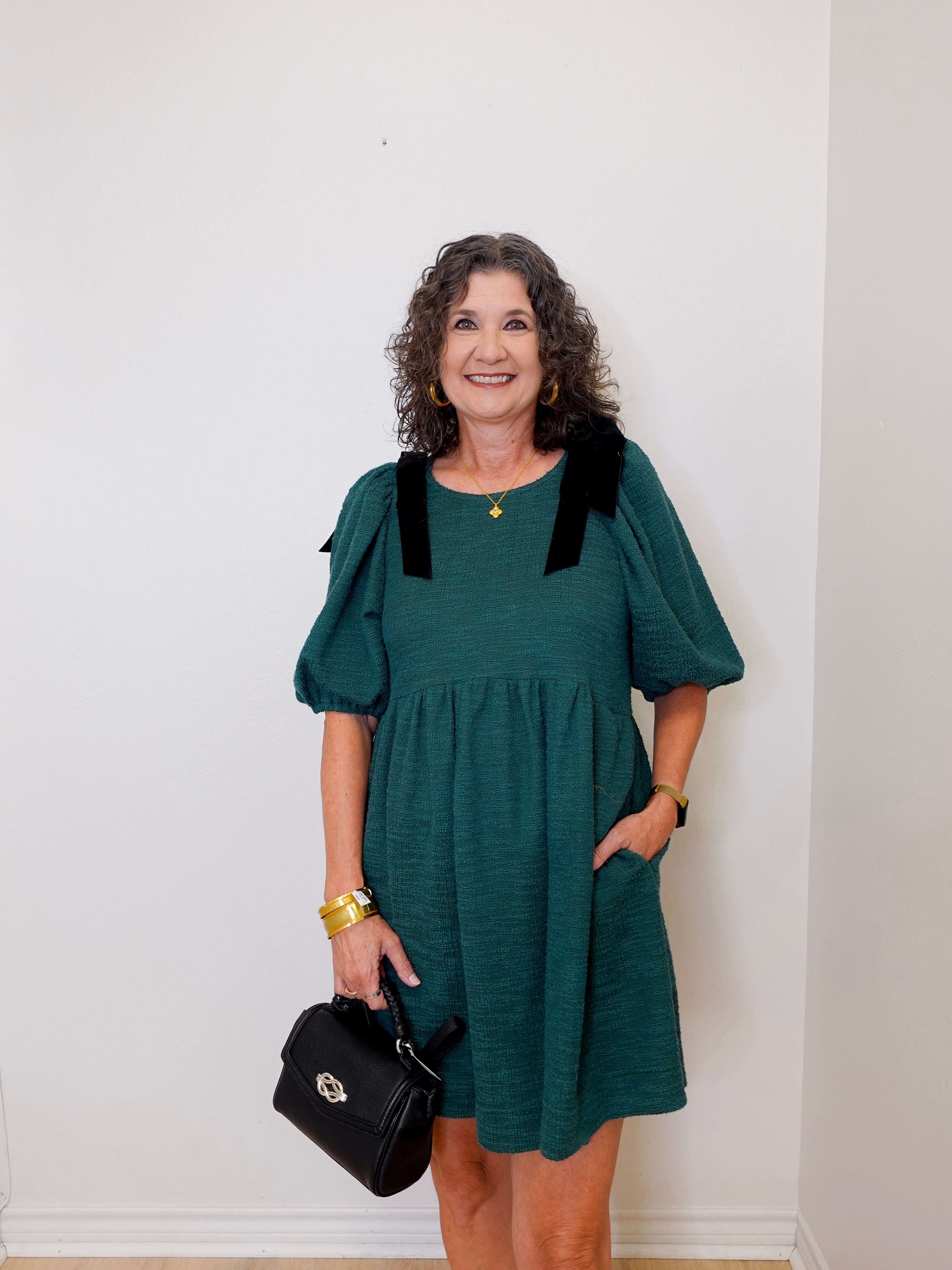 Woman wearing a teal dress with black accents against a white wall