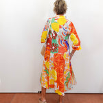 Person wearing a colorful floral dress standing against a white wall.