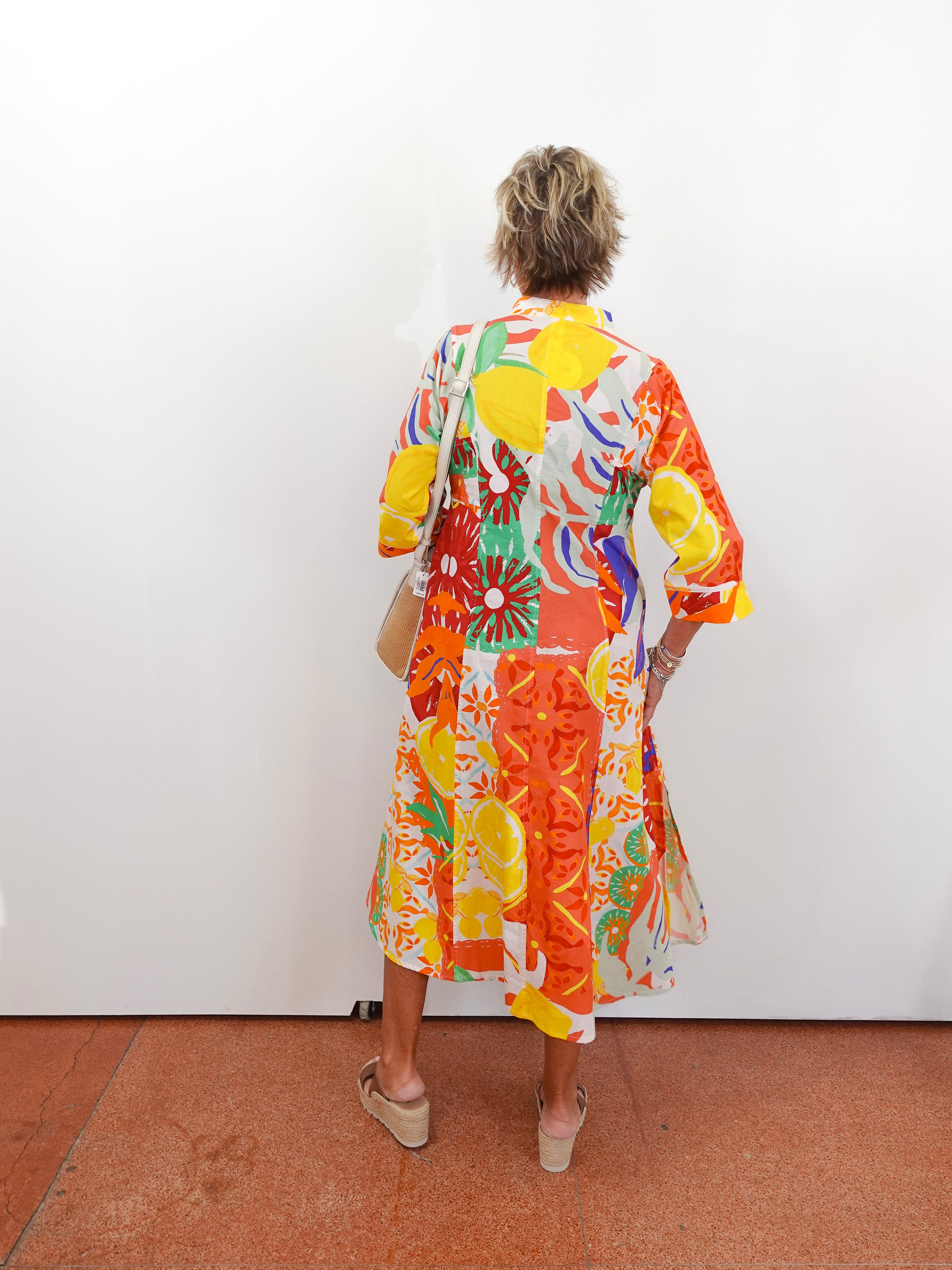 Person wearing a colorful floral dress standing against a white wall.