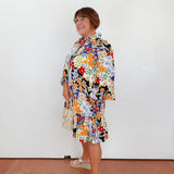 Woman wearing a colorful floral dress against a white wall.