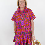 Woman wearing a colorful patterned dress holding a straw bag against a white background