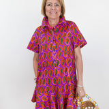 Woman wearing a colorful patterned dress holding a straw bag against a white background