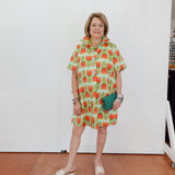 Woman wearing a colorful dress with a pattern of red and green shapes against a white wall.