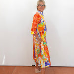 Person wearing a colorful dress standing against a white wall.
