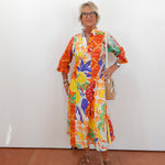 Woman wearing a colorful patterned dress against a white wall.