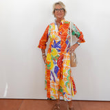 Woman wearing a colorful patterned dress against a white wall.