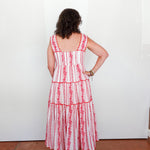Woman wearing a red and white striped dress with floral details, standing against a white wall.