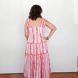 Woman wearing a red and white striped dress with floral details, standing against a white wall.