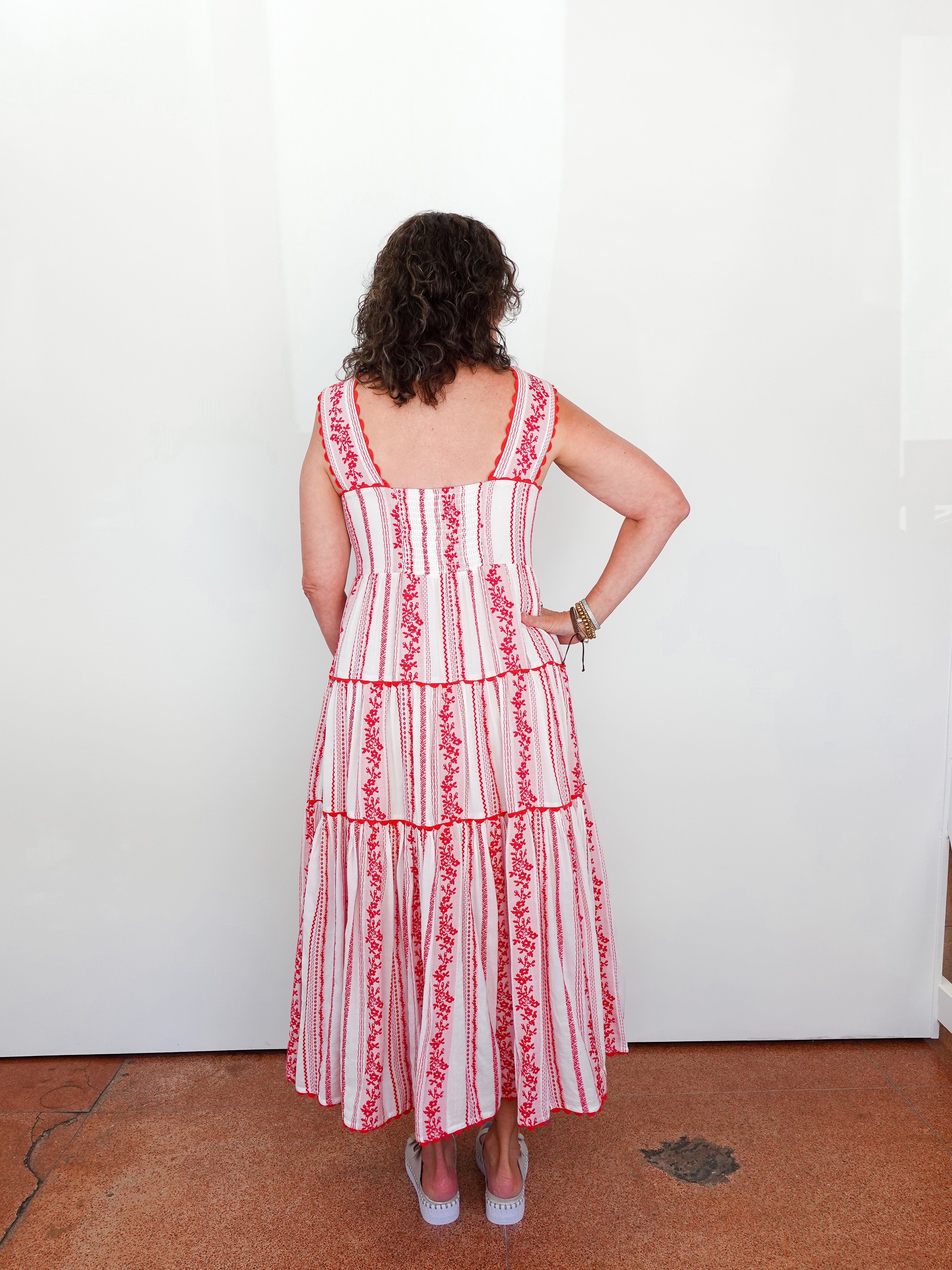Woman wearing a red and white striped dress with floral details, standing against a white wall.