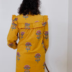 Person wearing a yellow dress with floral patterns against a white background