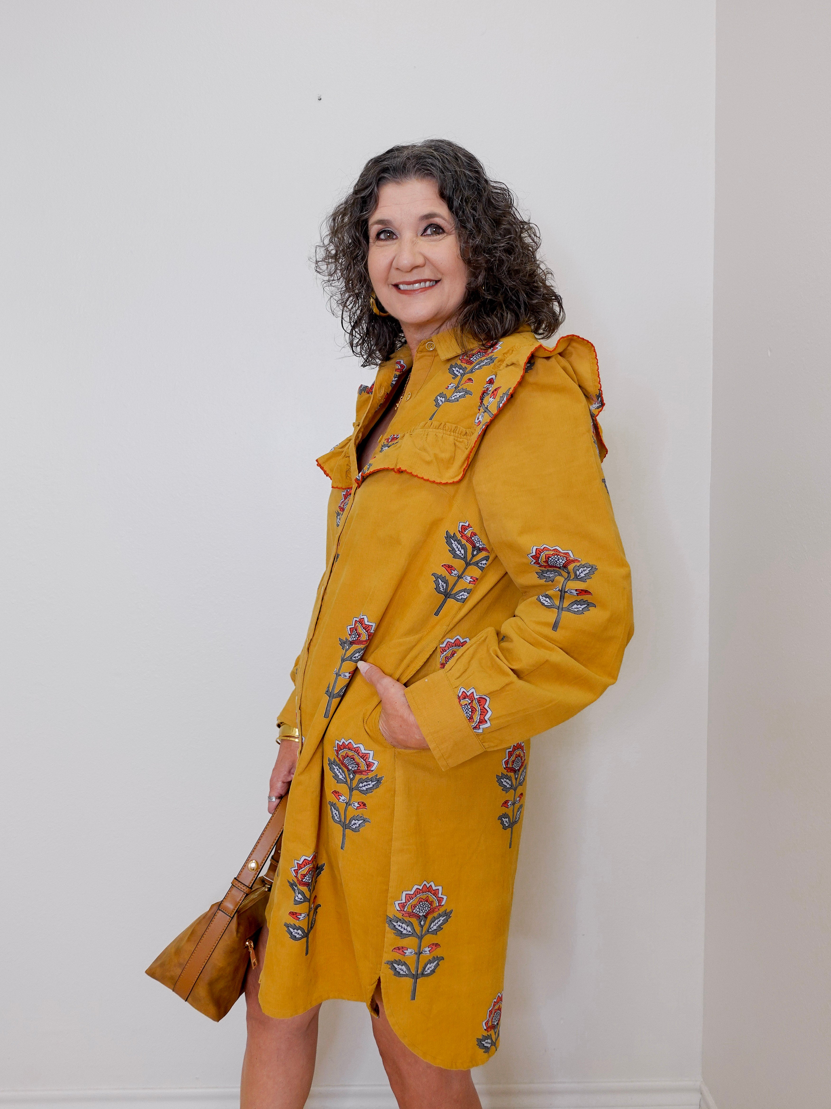Woman wearing a yellow coat with floral embroidery against a white wall