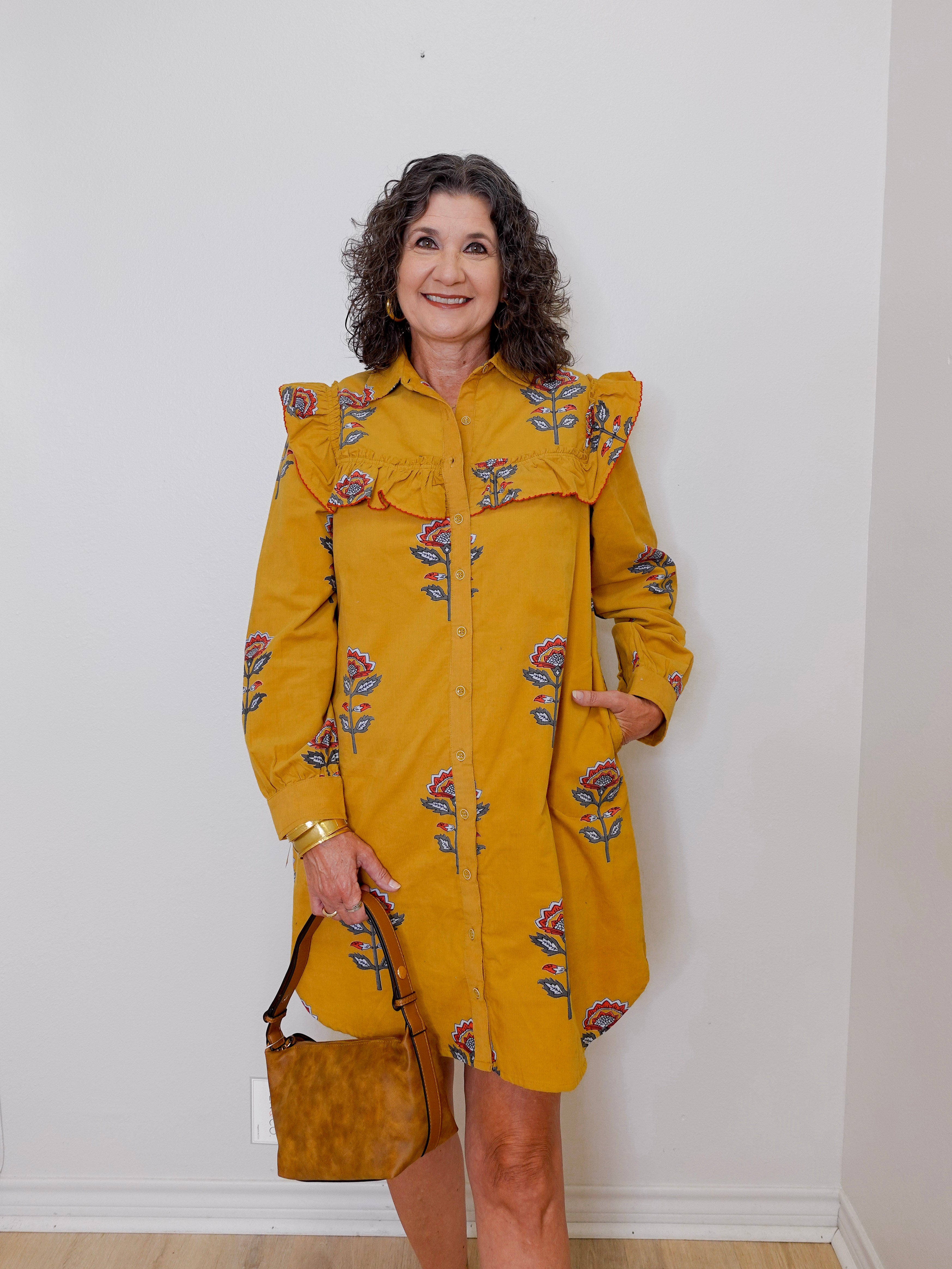 Woman wearing a yellow floral dress against a white wall