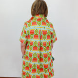 Person wearing a colorful patterned dress against a white wall.