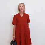 woman wearing a brick color tiered knit dress against a white background. 