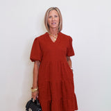 woman wearing a brick color tiered knit dress against a white background. 