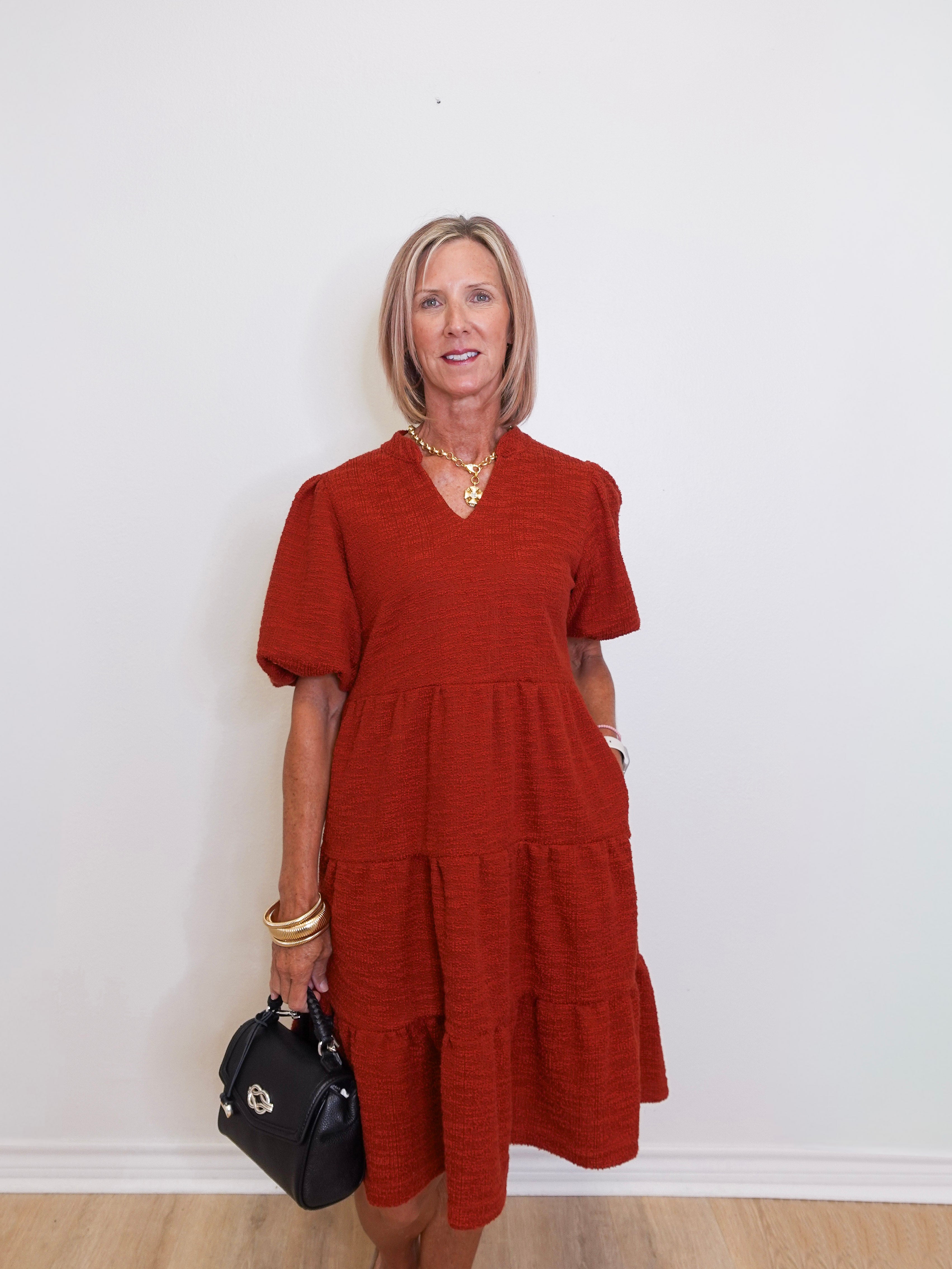 woman wearing a brick color tiered knit dress against a white background. 