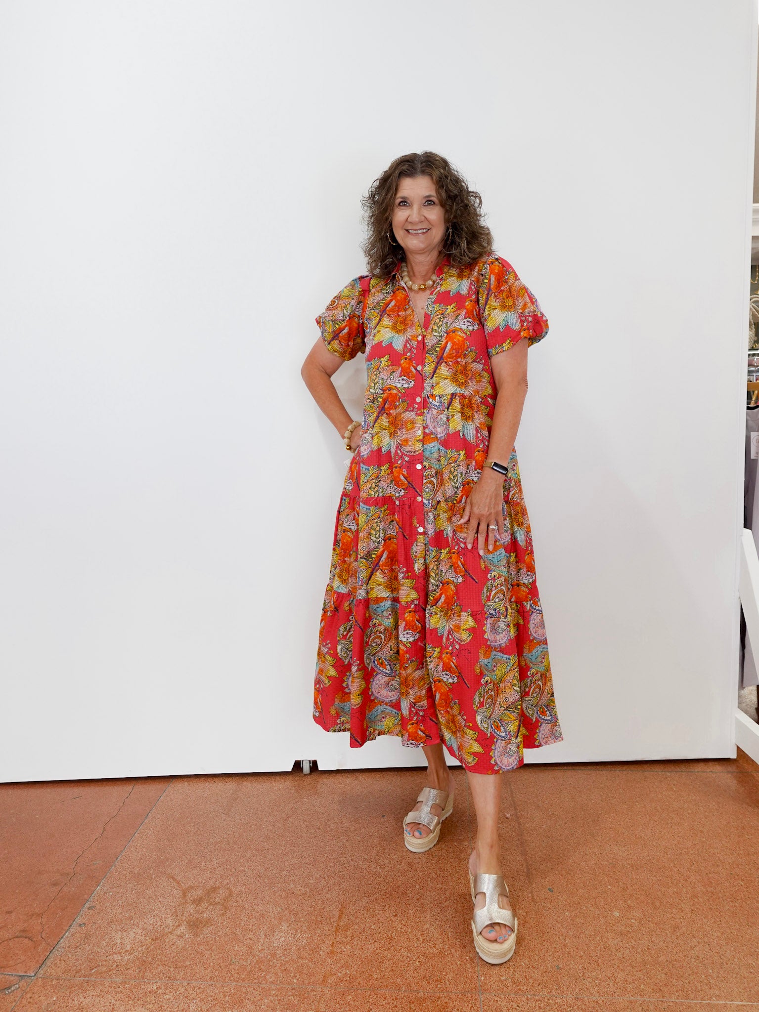 Woman wearing a colorful floral dress standing against a white wall.