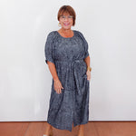 Woman wearing a blue dress standing against a white wall.