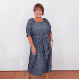 Woman wearing a blue dress standing against a white wall.