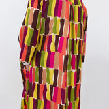 A long-sleeve button-up shirt with a colorful abstract geometric pattern of vertical brushstroke blocks in pink, orange, yellow, green, brown, and beige, shown from the back on a mannequin against a plain white wall.