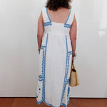 Person wearing a white dress with blue patterns, standing against a plain white wall.