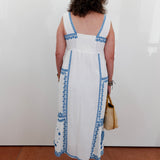 Person wearing a white dress with blue patterns, standing against a plain white wall.
