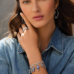 Woman wearing silver jewelry including earrings, ring, and bracelet against a neutral background