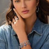 Woman wearing silver jewelry including earrings, ring, and bracelet against a neutral background