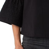Close-up of a person wearing a black blouse with smocked sleeves on a white background