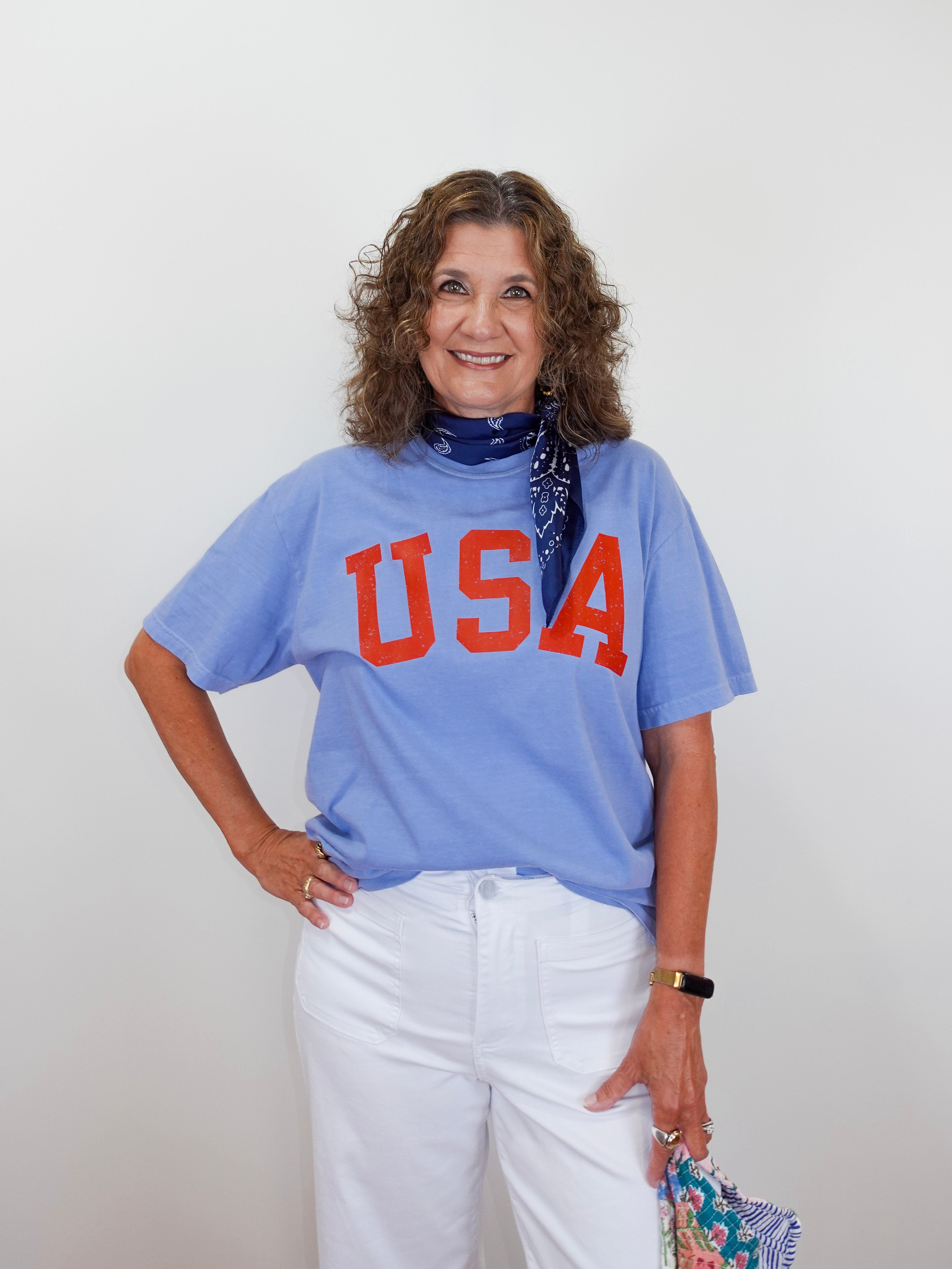 Woman wearing a blue 'USA' t-shirt with white pants against a plain background