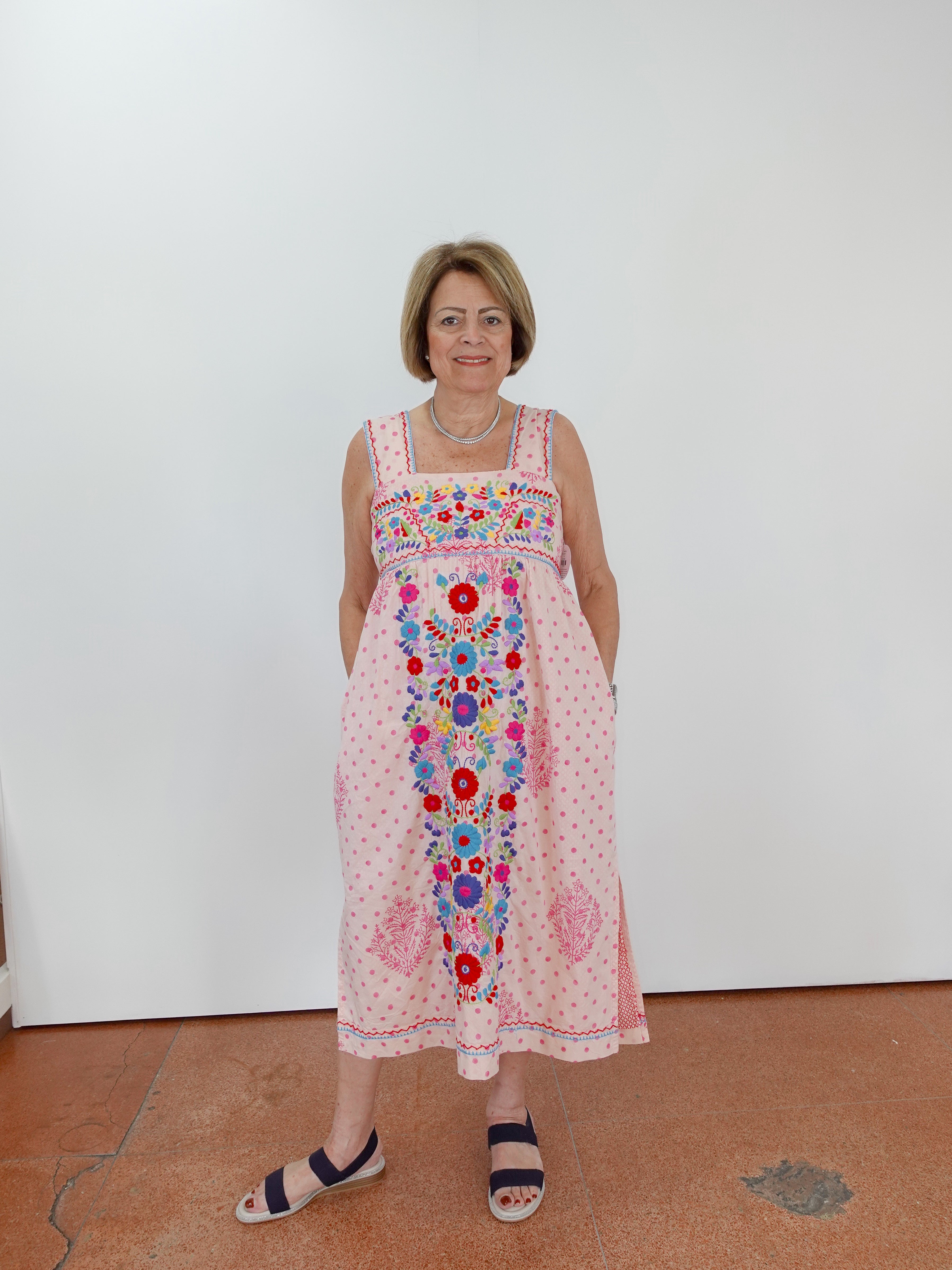 Woman wearing a colorful floral dress against a white wall.