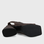 A single women's flat shoe shown from a side angle, featuring a dark brown woven strap and a black block heel with a black sole, set against a light gray background.