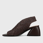 A dark brown woven slingback mule sandal with a chunky geometric block heel, shown from a side profile on a light gray background.