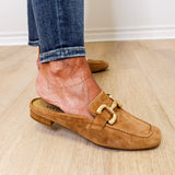 Brown suede loafer worn with rolled-up jeans on a wooden floor.